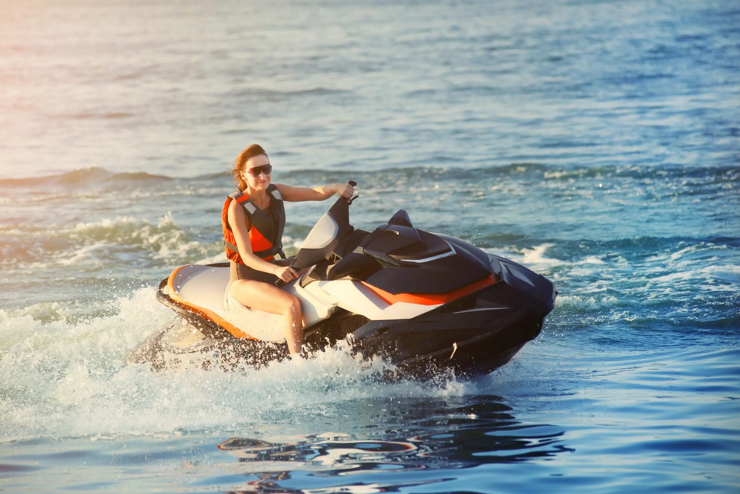 Young adult sporty caucasian woman riding jet ski in ocean blue water at warm evening sunset. Beach extreme sport activities and recreation in Marco Island